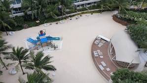 A resort with a sandy beach, palm trees, a pool area, and a deck with lounge chairs. - Family Condo by IA at Azure Urban Resort Residences (Parañaque)