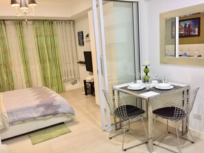 Quarto de hotel com uma cama, uma mesa de jantar com cadeiras, uma televisão e uma janela com um quadro.