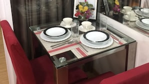 A dining area with a glass table set for two, red upholstered chairs, and a framed picture of flowers on the wall. - Family Condo by IA at Azure Urban Resort Residences (Parañaque)