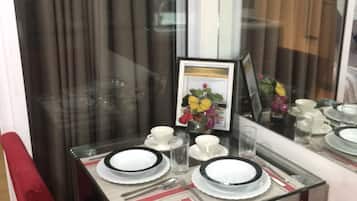 A dining area with a glass table set for two, red upholstered chairs, and a framed picture of flowers on the wall.