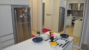 A modern kitchen with stainless steel appliances, a dining area with a white table set with plates and bowls, and a red carpet. - Studio M City Jalan Ampang by Fervent (Kuala Lumpur)