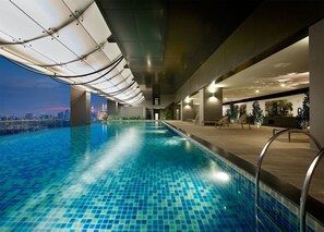 An indoor swimming pool with a cityscape view, modern architecture, and a poolside area with seating. - Studio M City Jalan Ampang by Fervent (Kuala Lumpur)