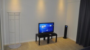A living room with a flat-screen TV on a black stand, a white floor lamp, and a black speaker. - Studio M City Jalan Ampang by Fervent (Kuala Lumpur)