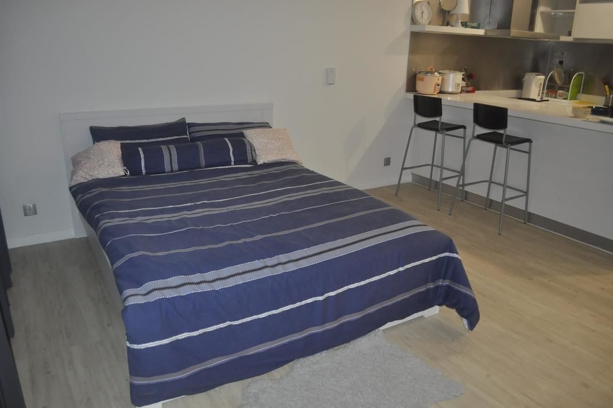 Un dormitorio con cama, una kitchenette pequeña y dos taburetes de bar.