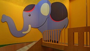 A children's play area with a slide, a wooden bench, and a wall mural of an elephant. - Romantic Code Motel (Tainan)