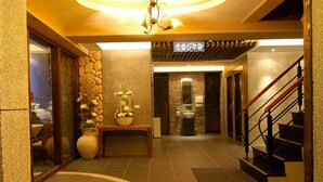 A hotel lobby with a stone wall, a reception desk, a staircase, and a sign indicating amenities. - Romantic Code Motel (Tainan)