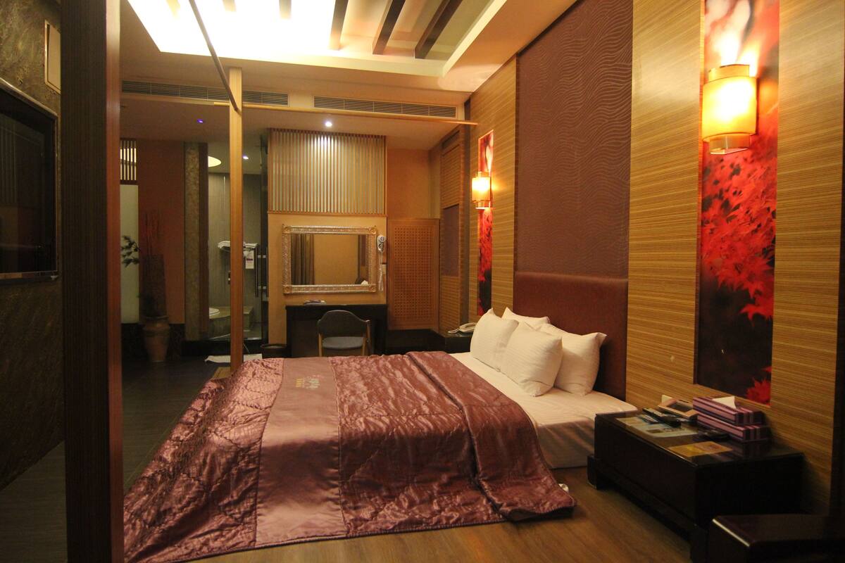 Quarto de hotel com uma cama grande, uma escrivaninha, uma cadeira e uma mesa de cabeceira.