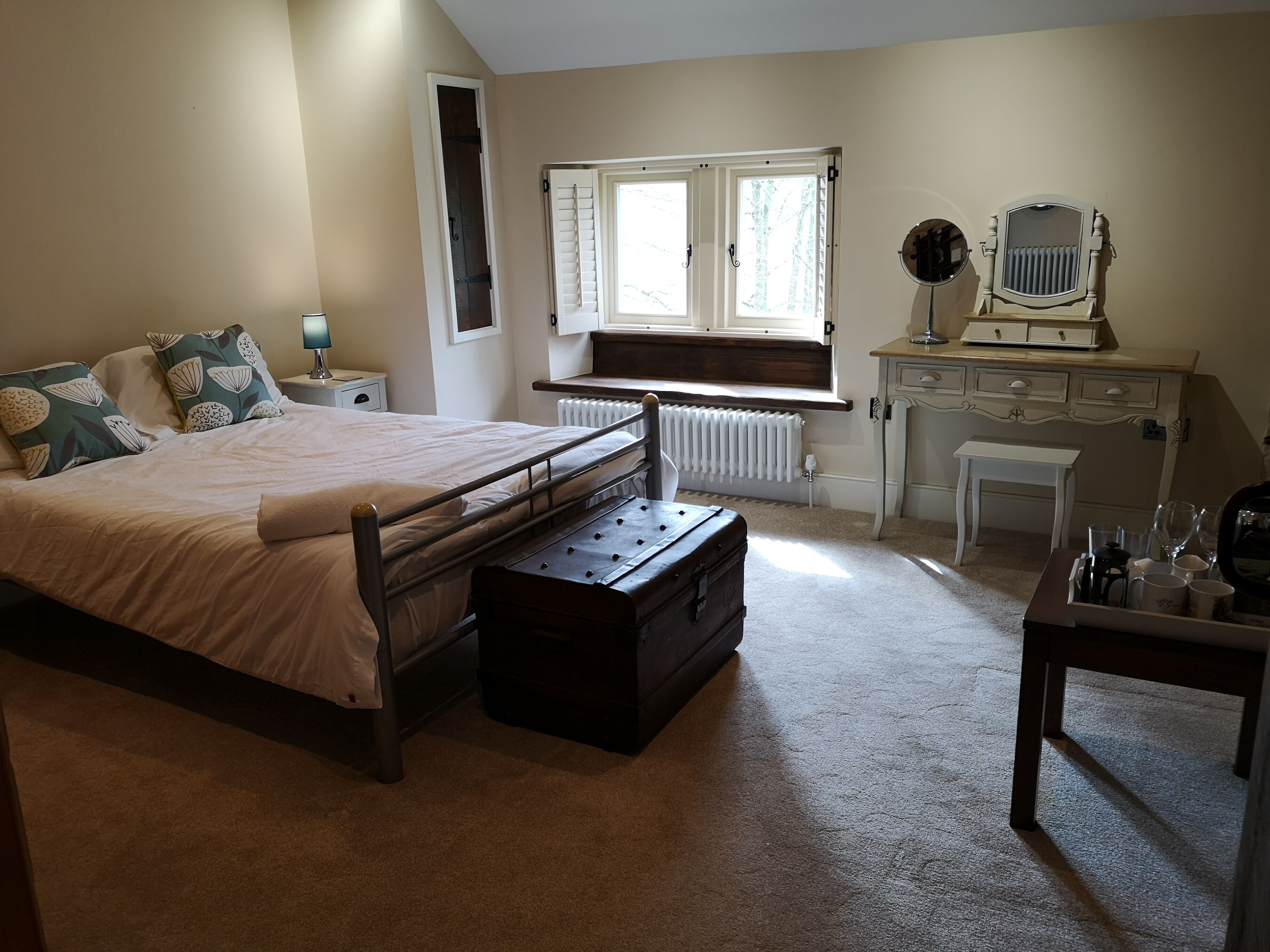 A bedroom with a bed, dresser, vanity, and a window with shutters.