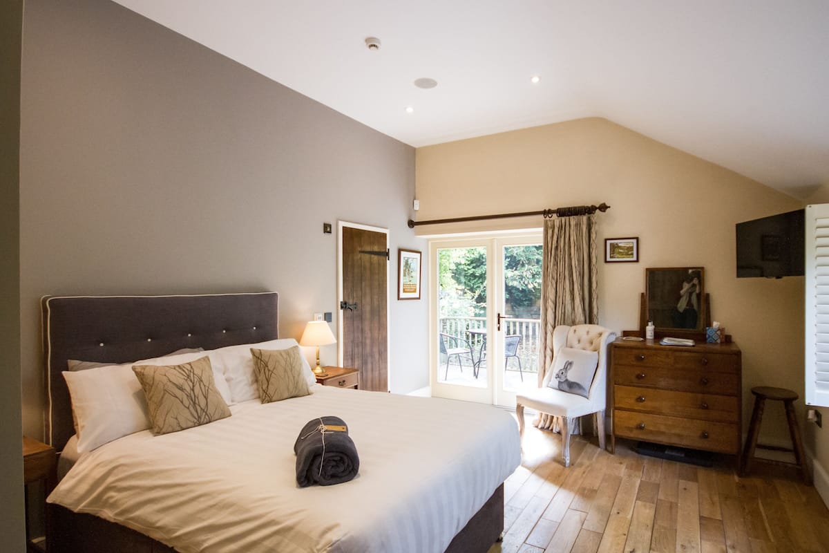 A bedroom with a large bed, a dresser, a chair, and a balcony with outdoor furniture.