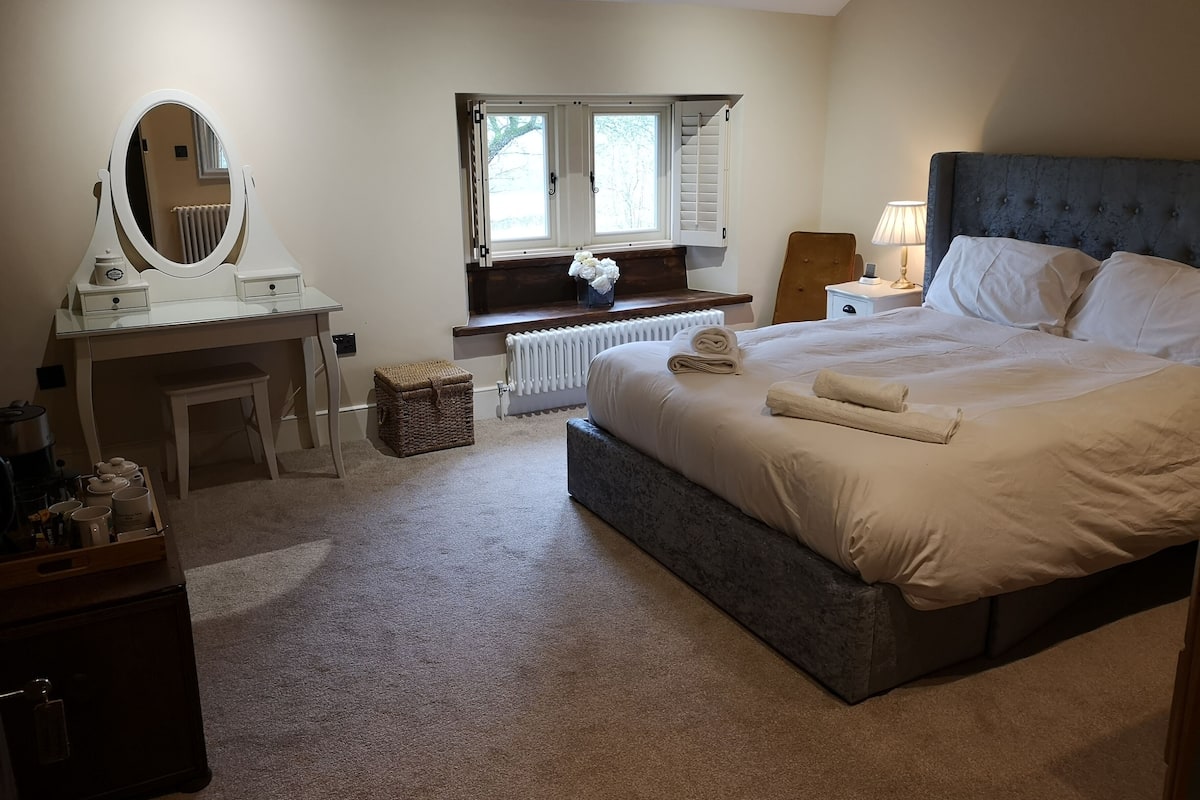A bedroom with a bed, a bedside table, a dresser, a mirror, a window, and a radiator.
