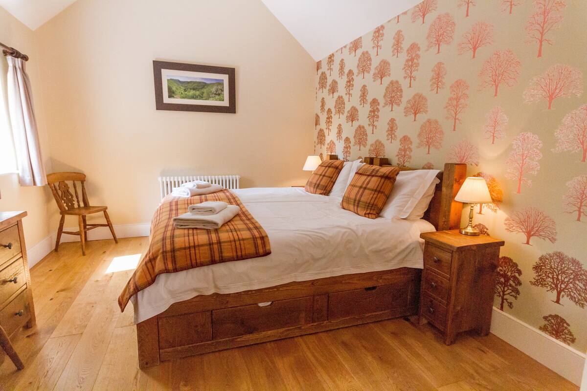 A bedroom with a wooden bed, a chair, a radiator, and a wall with tree patterns.