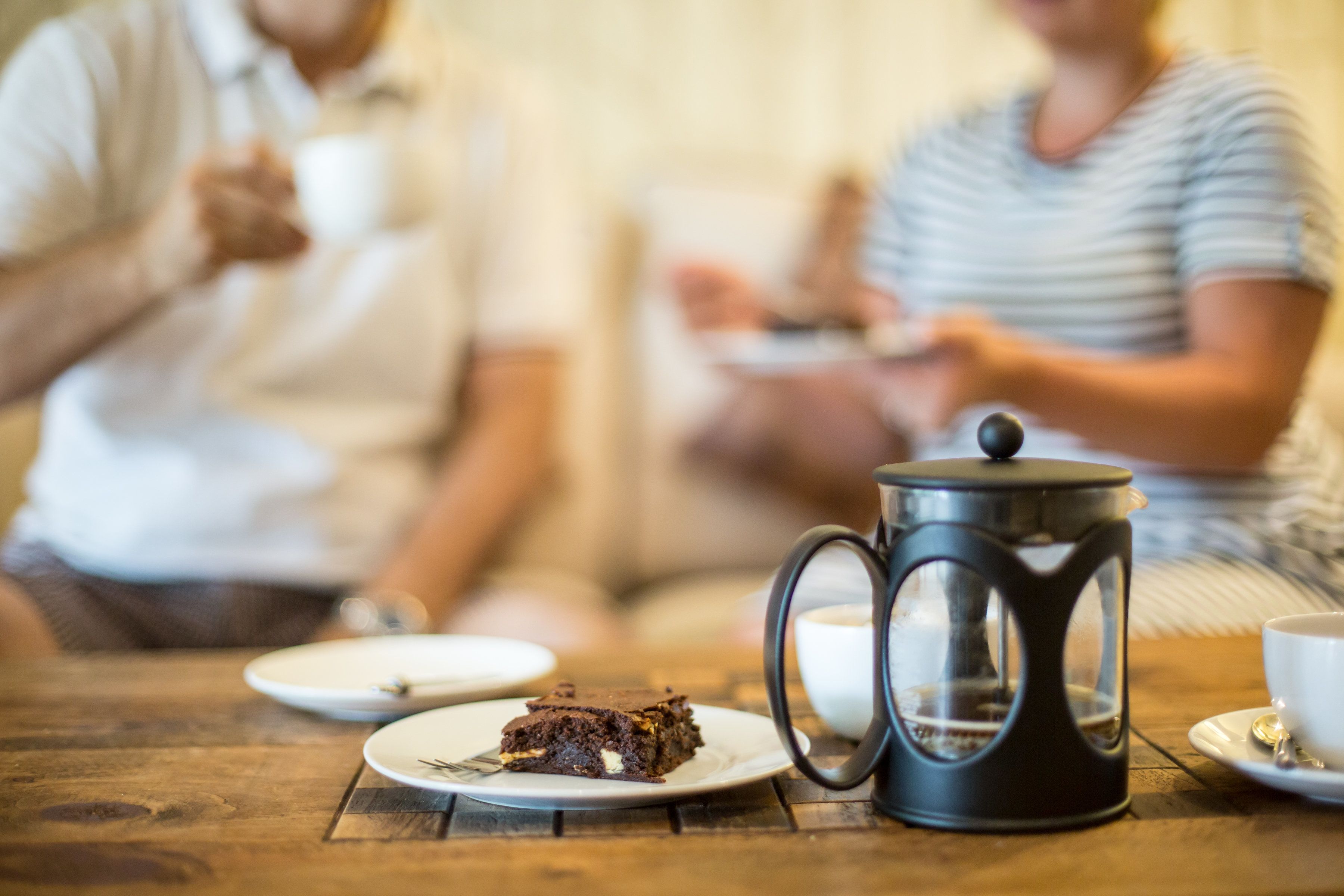 A wooden table with a coffee pot, a plate with a slice of cake, and a cup.