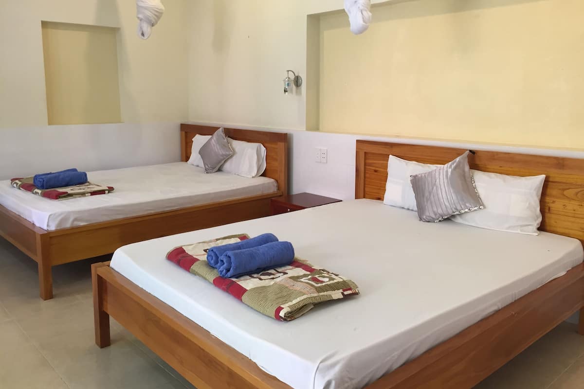 Duas camas de solteiro com estrutura de madeira e roupa de cama branca, cada uma com uma toalha enrolada e um cobertor estampado.