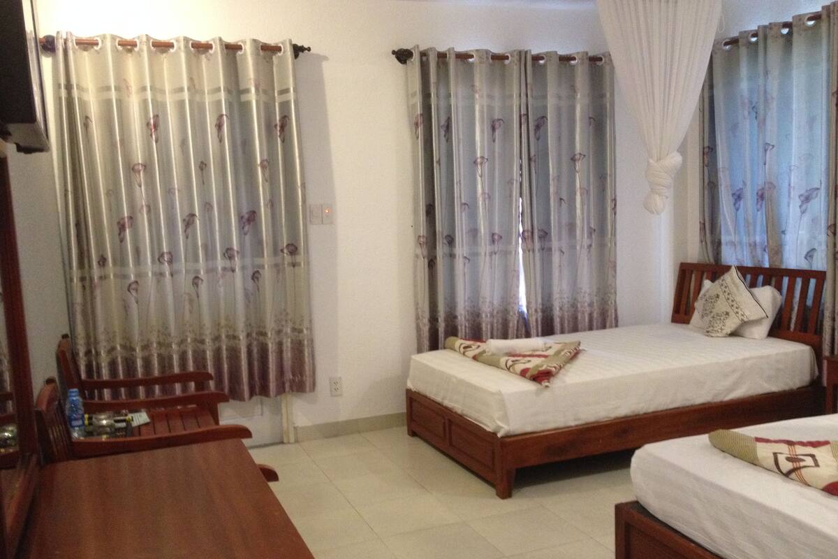 Quarto com duas camas, uma mesa de madeira e cortinas.