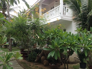 A garden with various plants and a white building with a balcony. - Nhat Quang Family Beach (Mui Ne)