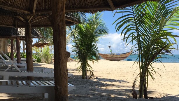 Un área de estar junto a la playa con bancos de madera y una estructura de techo de paja.