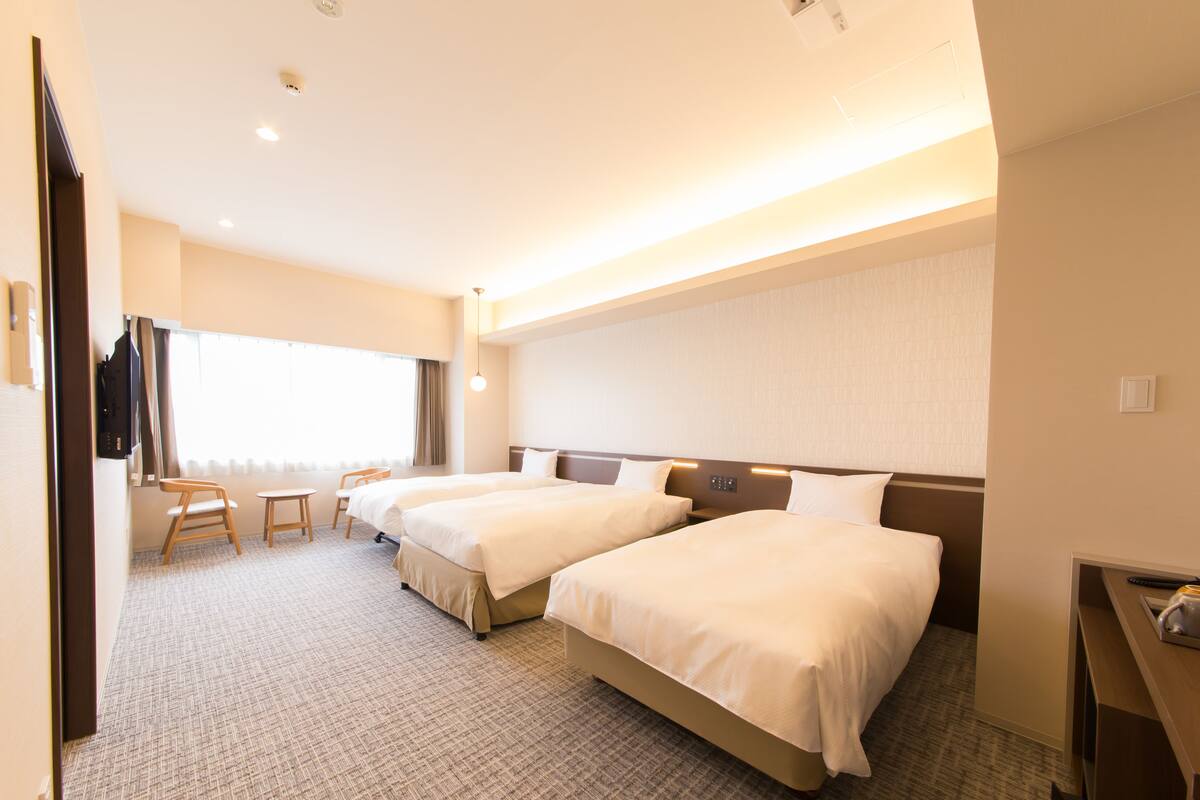A hotel room with two beds, a desk, a chair, and a large window.
