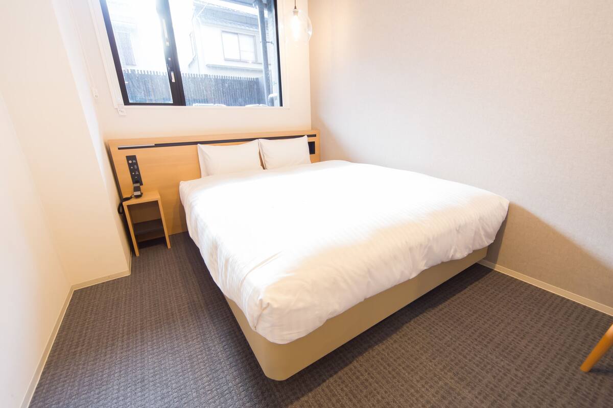 A hotel room with a single bed, a nightstand, a window, and a carpeted floor.