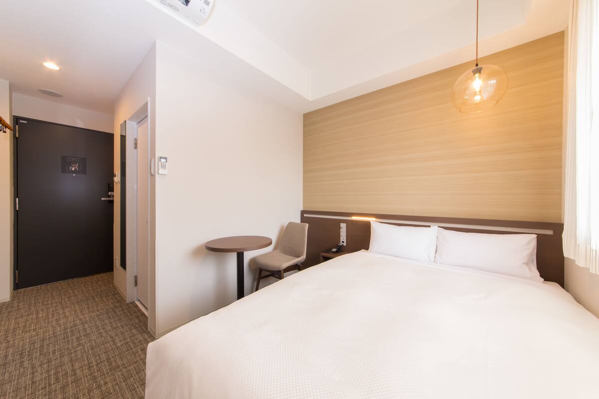 A hotel room with a large bed, a small table, a chair, and a wooden headboard.