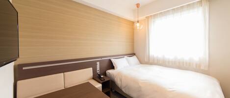 A hotel room with a bed, bedside table, and a TV mounted on the wall.