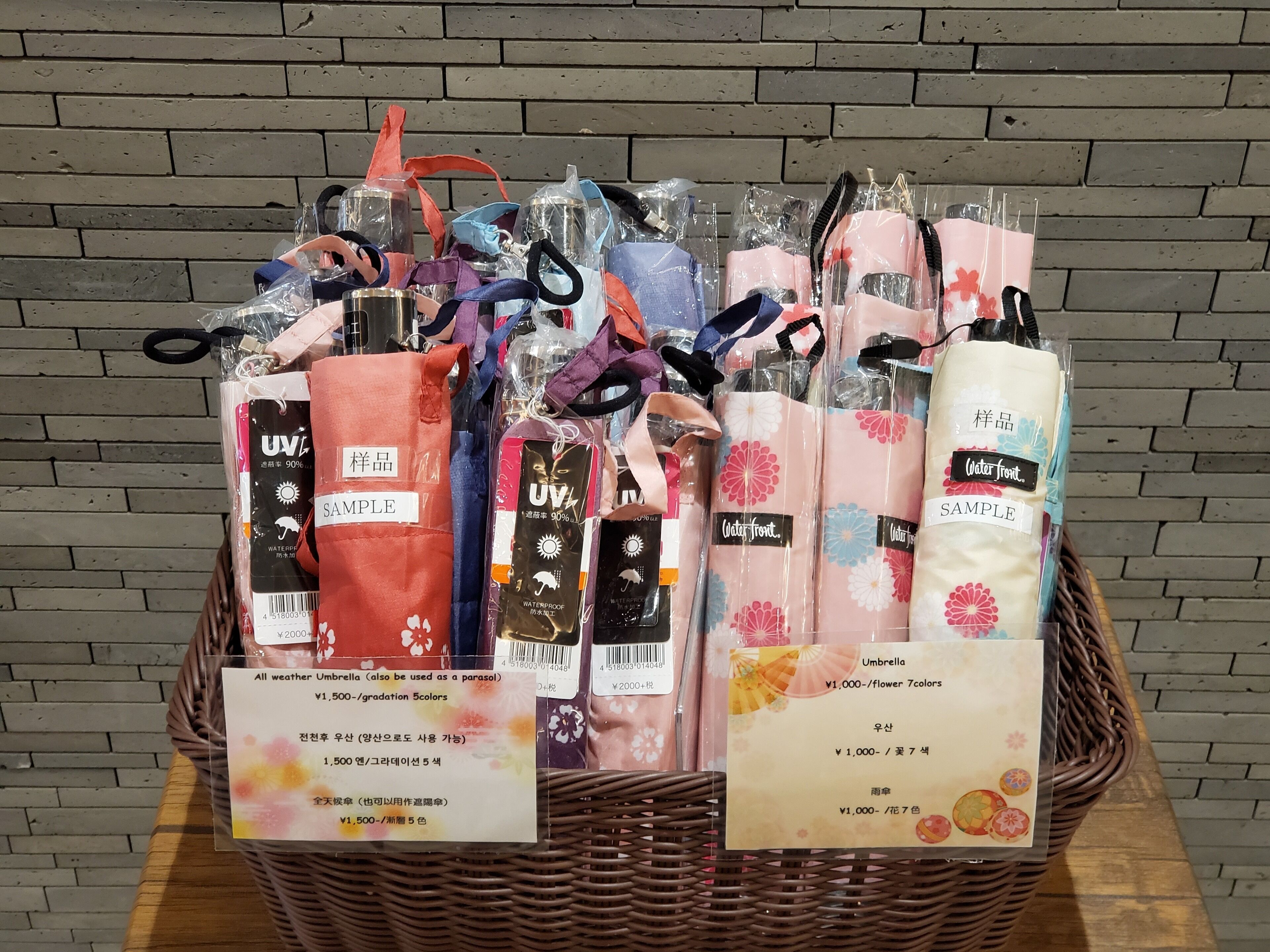 A basket filled with various umbrellas and raincoats, some labeled with "UV" and "waterproof" features, and price tags indicating different colors and prices.
