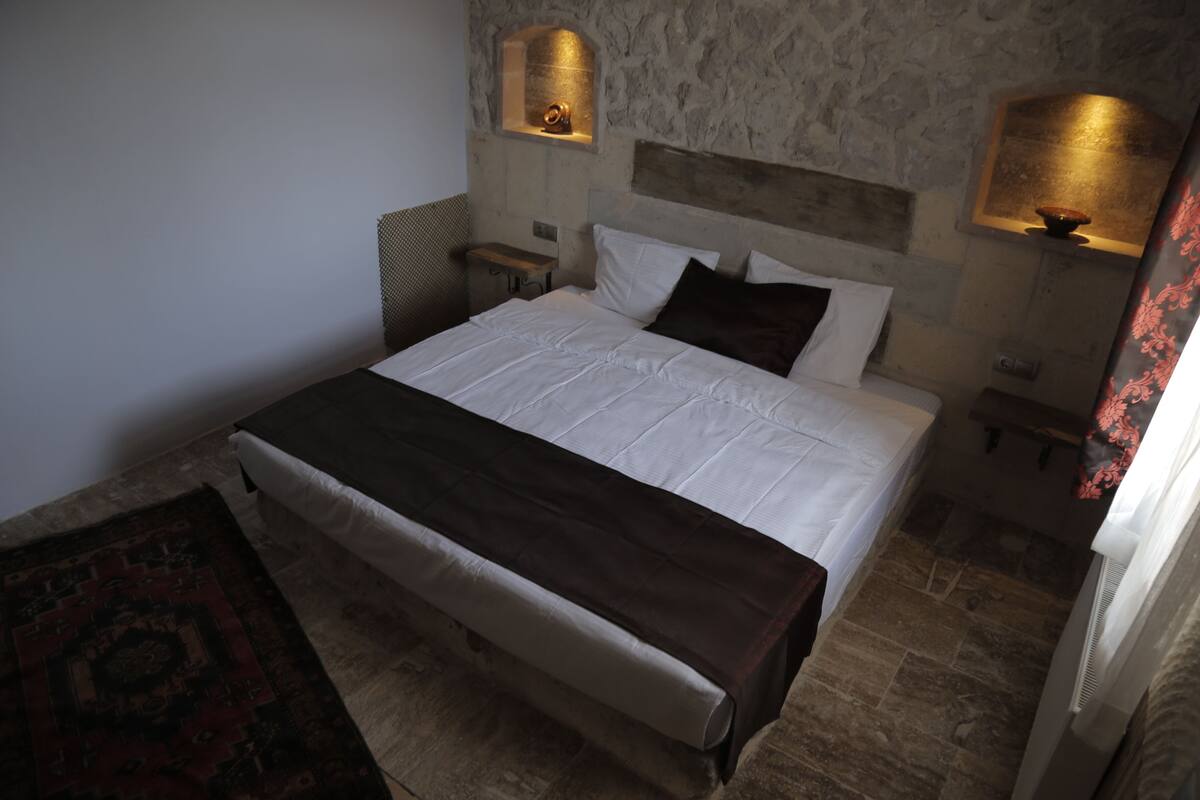 A bedroom with a large bed, stone walls, and two wall-mounted lamps.