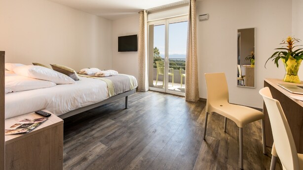 Ein Hotelzimmer mit Bett, Schreibtisch, Stuhl, Fernseher und einem Balkon mit Blick.