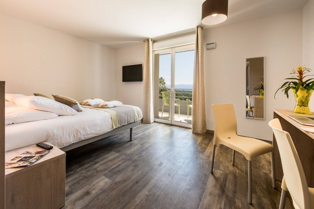A hotel room with a bed, a desk, a chair, a TV, and a balcony with a view.