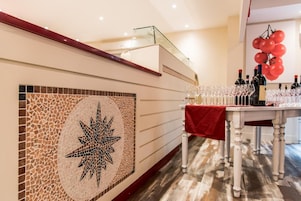 Uma área de recepção com um painel de mosaicos, uma escadaria e uma mesa com garrafas de vinho e copos.