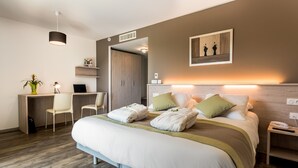 Ein modernes Hotelzimmer mit einem großen Bett, Nachttischen, einem Schreibtisch mit Stuhl, einer Pflanze und einem Bild an der Wand.