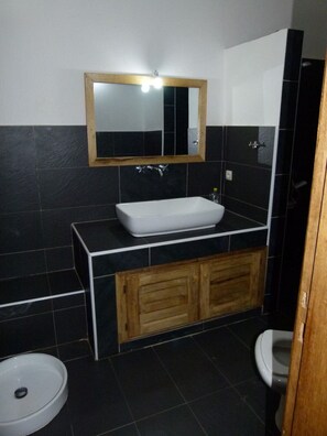 A bathroom with a white sink, wooden vanity, black tiled walls, and a mirror with lights. - Villa dallie Senegal (Mbour)