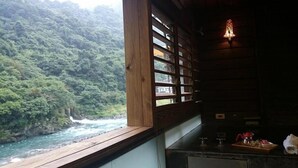 A rustic cabin with a wooden interior, a window overlooking a river, and a small kitchenette with a coffee maker and jars. - 51 Spring (New Taipei City)
