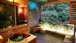 A bathroom with a wooden interior, a stone wall, a large window with a view of trees, and a bench. - 51 Spring (New Taipei City)