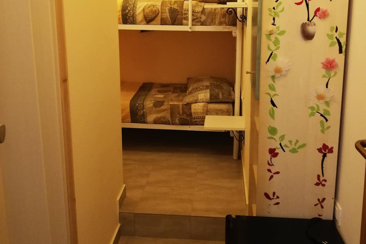 A narrow hallway with a bunk bed in the background, a door with floral decals, and a black storage box on the floor.