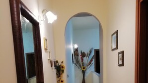 Un pasillo estrecho con un espejo, un teléfono y un jarrón con girasoles.