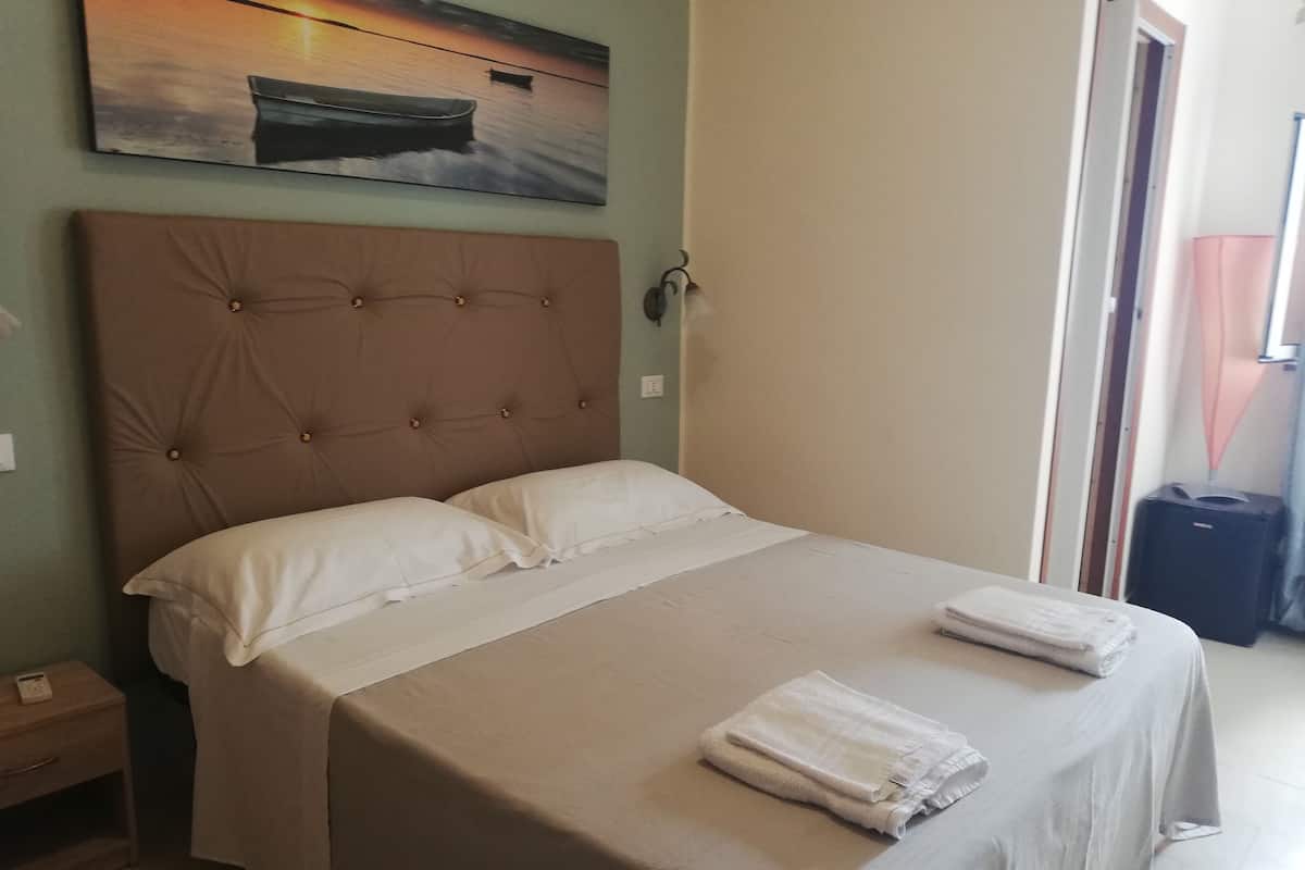 A neatly made bed with a headboard, a bedside table with a lamp, and a painting on the wall.