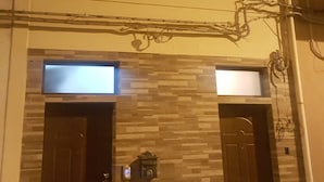 Un edificio de dos pisos con un balcón en el nivel superior, una puerta con buzón y una pared con diseño decorativo.