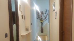 Un pasillo con una puerta de madera a la derecha, un espejo a la izquierda y un jarrón con ramas y un girasol en el centro.