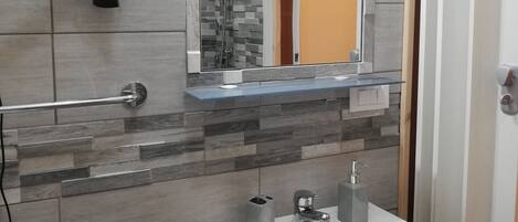 Un baño con lavamanos blanco, espejo, secador de pelo y ducha.