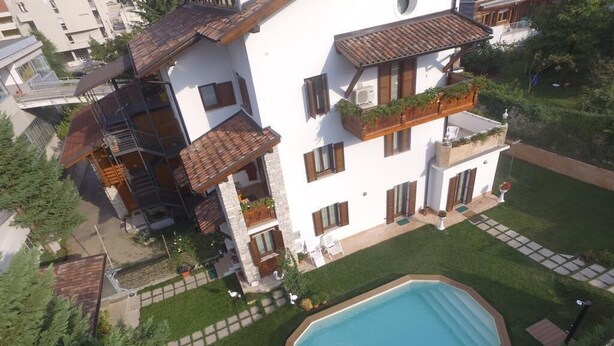 A multi-story residential building with a swimming pool, balconies with plants, and a well-maintained lawn. - Le Cicogne (Rovereto)