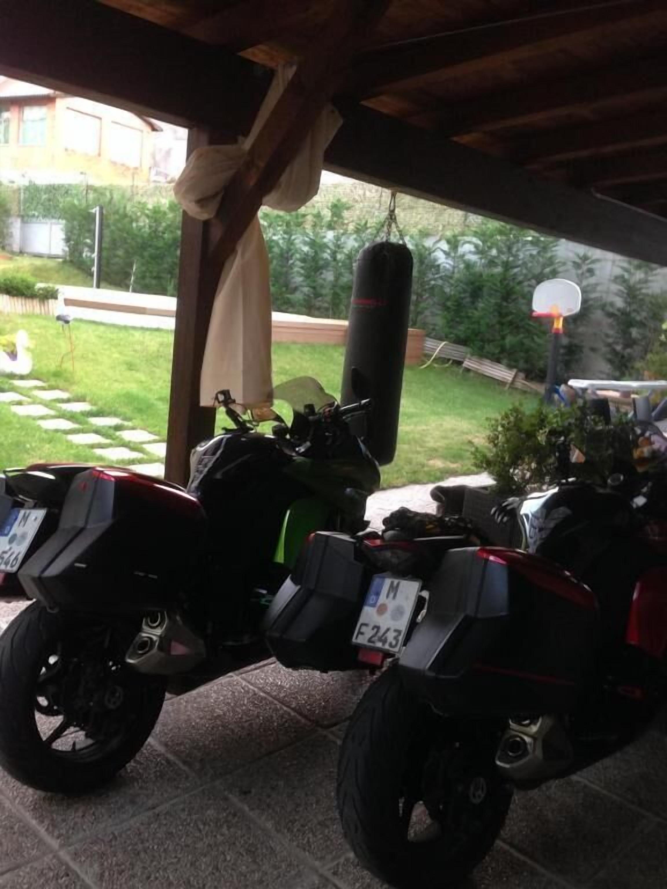 Two motorcycles parked under a covered area with a garden view.