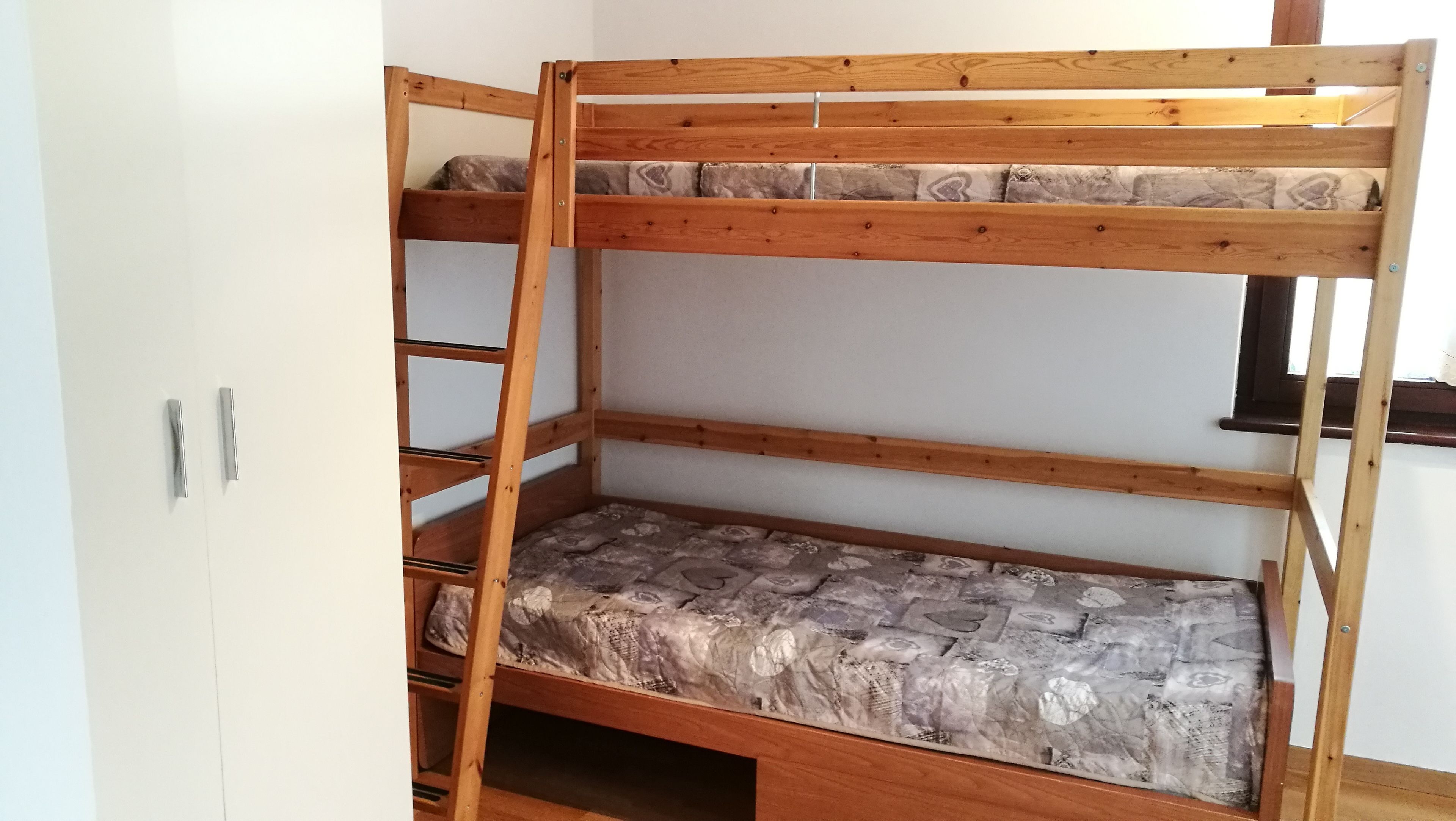 A bunk bed with a mattress featuring a stone-like pattern, a wooden ladder, and metal handles on a white wardrobe.