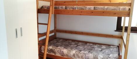 A bunk bed with a mattress featuring a stone-like pattern, a wooden ladder, and metal handles on a white wardrobe.