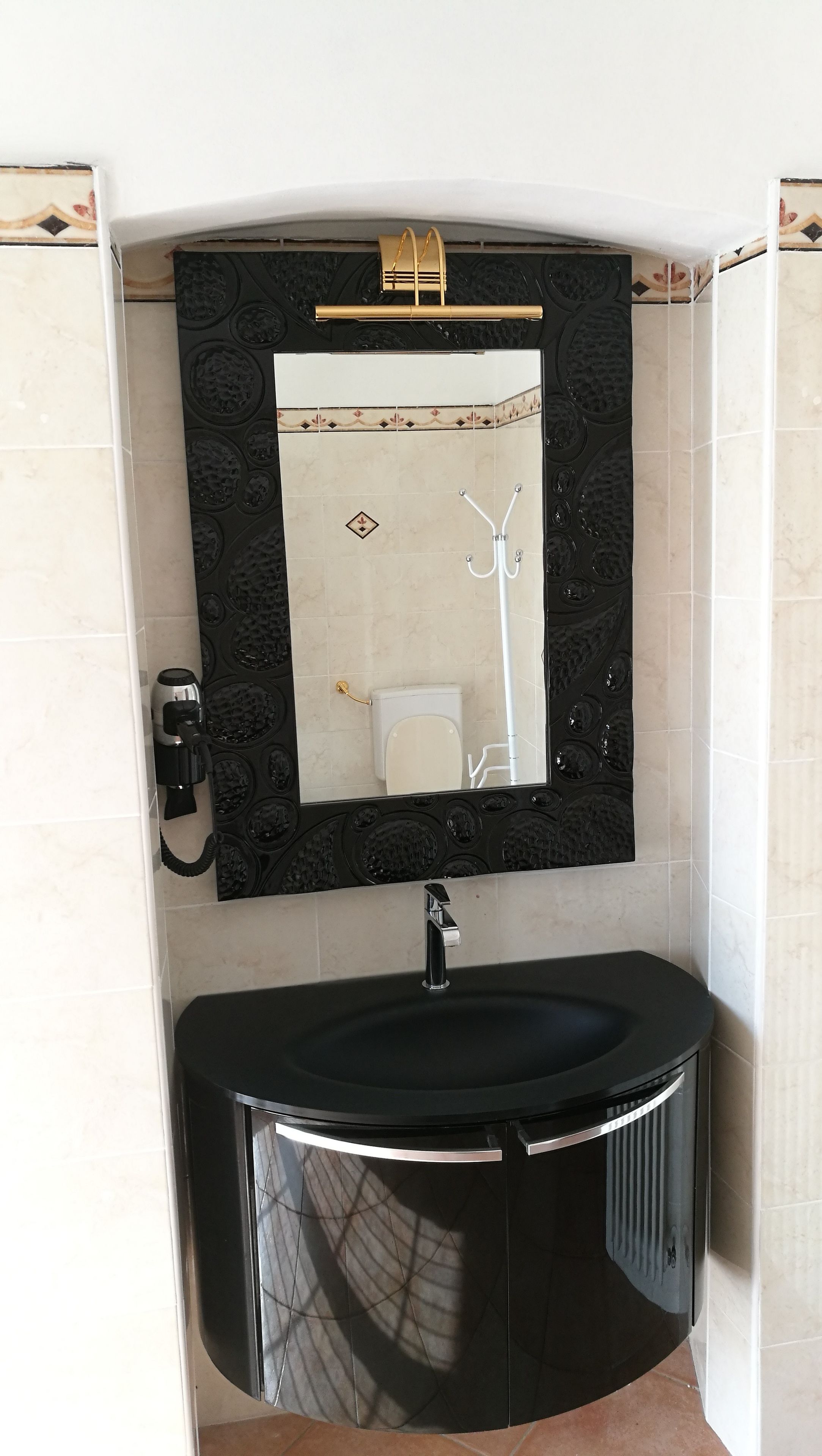 A bathroom with a black vanity, a white toilet, and a mirror with a decorative frame.