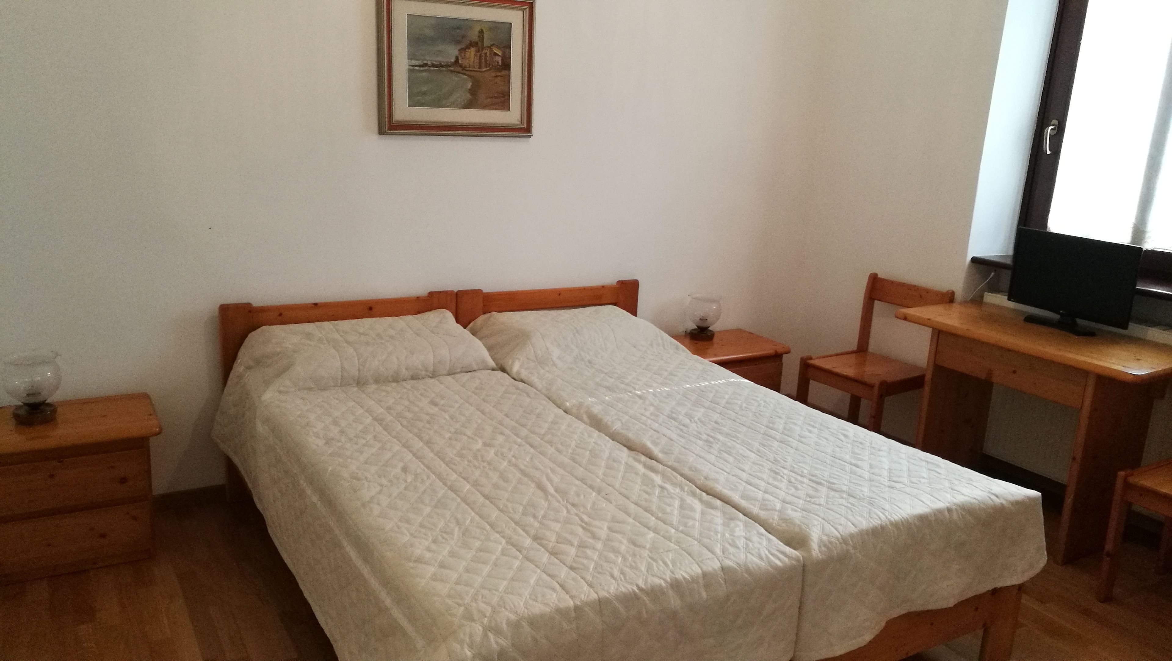 Une pièce simple comprenant un lit, un bureau avec une chaise, un téléviseur et une petite table avec un verre.