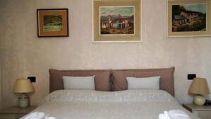 A hotel room with a large bed, two pillows, a nightstand with a lamp, and a wall with three framed pictures. - Le Cicogne (Rovereto)