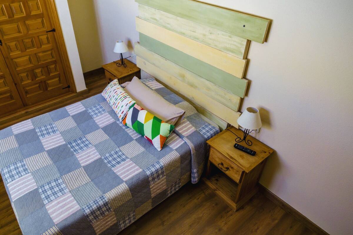 A bedroom with a wooden bed, a quilt, a pillow, two bedside tables with lamps, and a wooden wardrobe.