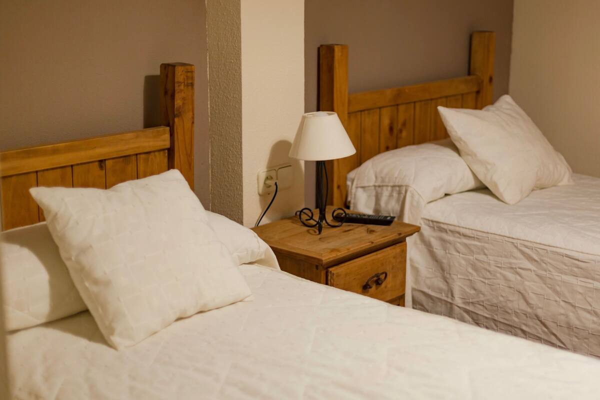 Two single beds with wooden headboards, white bedding, and a bedside table with a lamp and remote control.