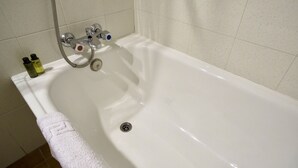 A white bathtub with a shower head and two faucets, a towel, and two bottles of shampoo and conditioner. - Hotel La Gerencia (Checa)
