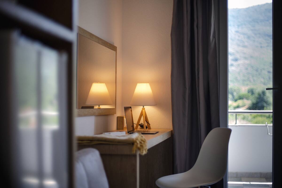 Ein Hotelzimmer mit Schreibtisch, zwei Lampen, einem Sessel und Blick auf einen Berg.